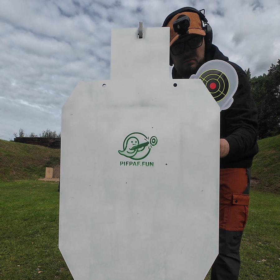 Instruktor w ochronie oczu i słuchu stoi za metalową sylwetką z logo PifPaf.fun i ręką wychyla na bok okrągłą głowę tarczy z tarczką